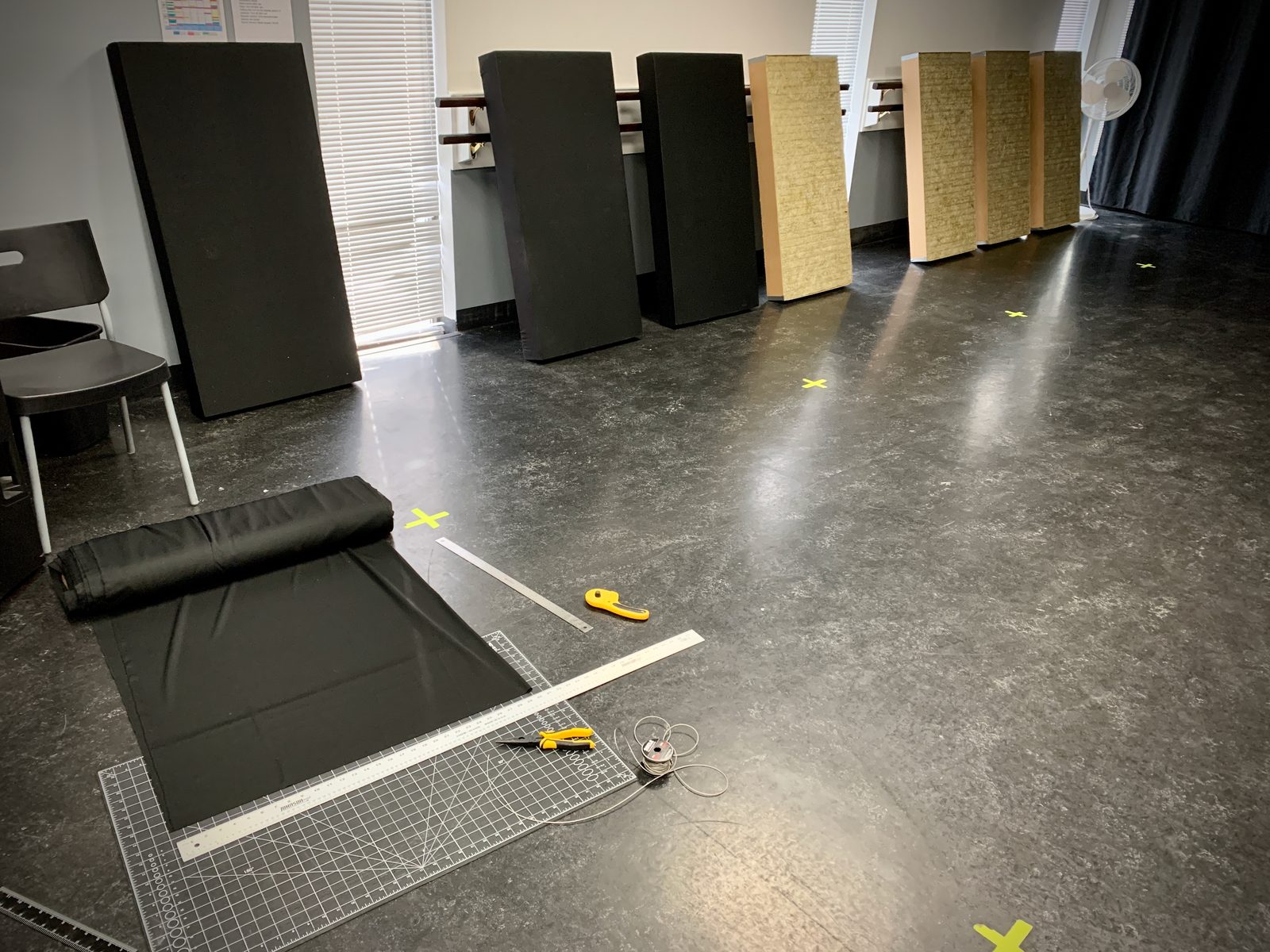 Studio 12 acoustic panels being built, with a cutting mat, ruler and rotary cutter next to raw stone-wool cores and finished fabric-faced panels