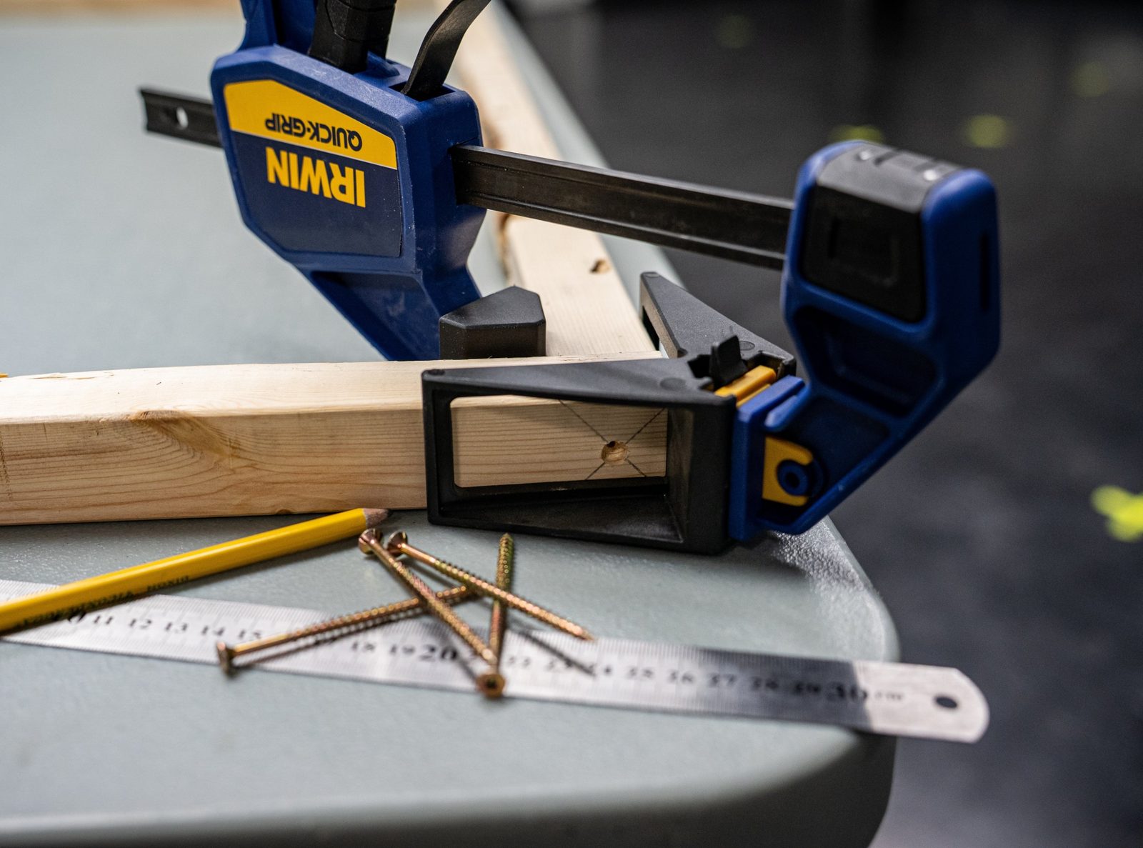 A solid-wood frame piece clamped during construction of a Studio 12 acoustic panel, with a pencil and screws on the workbench